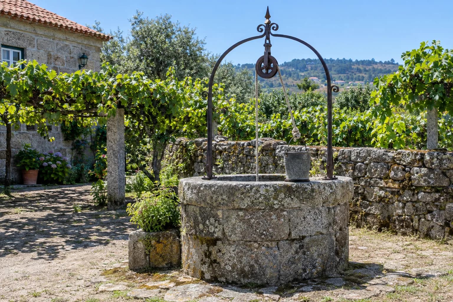 Poço de água redondo, de pedra de granito, com um arco de ferro e uma roldana, numa quinta do norte de Portugal